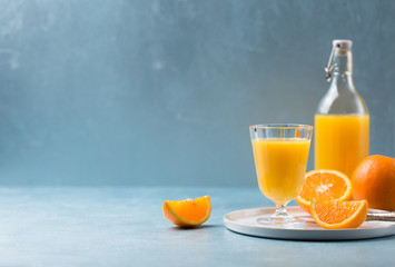 Glass of fresh orange juice with orange slices on white plate, blue background, cold summer refreshing nutritional beverage, blue orange color contrast, vitamin C healthy drink, copy space