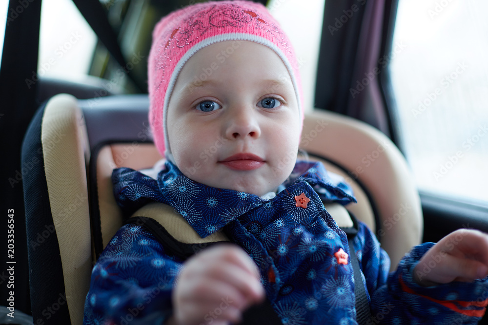 little girl with blue eyes sitting in a child seat in the back seat of ...