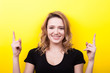 Happy smiling woman pointing up on yellow background in studio photo