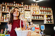 Girl in red holding different products on basket at deli store.