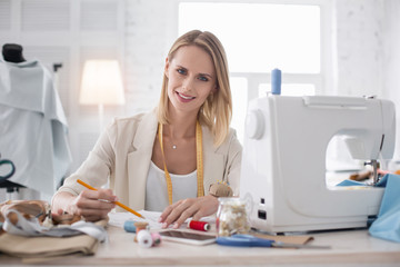 Wall Mural - Exceptional talent. Exuberant female couturier smiling to camera while sketching