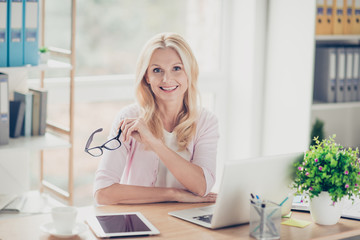 Nice, cute, friendly, aged, experienced financier, holding glasses in hand, having laptop, tablet on the table, looking at camera, sitting at desktop in work place