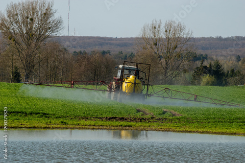 Fotografía Farmer on tractor spraying green wheat field