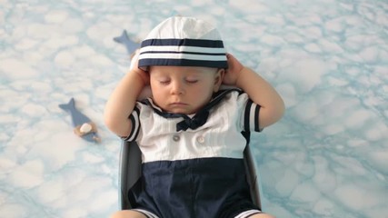 Wall Mural - Cute toddler baby boy sleeping in wooden boat with fishes, starfish and binoculars, dressed as sailman, indoors shot