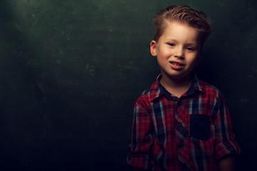 cute smiling little boy wearing red stylish shirt stands in dark corner, copyspace