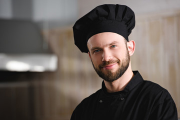 Canvas Print - portrait of handsome chef in black uniform looking at camera at restaurant kitchen