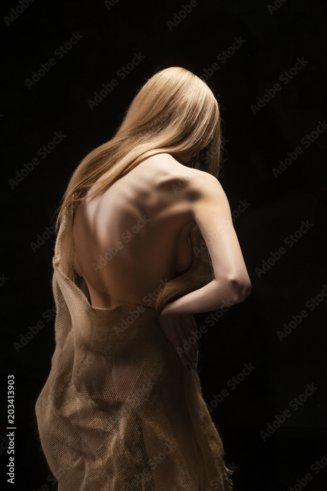 A beautiful young big breasted naked blonde girl, covering her nakedness with a cloth of burlap
