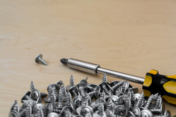 group of silvery self-tapping screws is arbitrarily positioned on a wooden surface, selective focus, abstract background