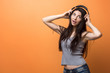 © merrymirta - Portrait of a young girl listening to the music through the headphones and holding it in her hands against orange background. Lifestyle, people and technologies concept