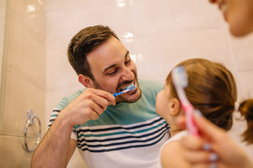 Wall Mural - Young couple and their cute little daughter brushing teeth in bathroom