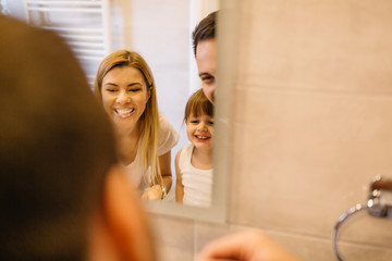 Wall Mural - Young couple and their beautiful daughter brushing teeth near mirror in bathroom