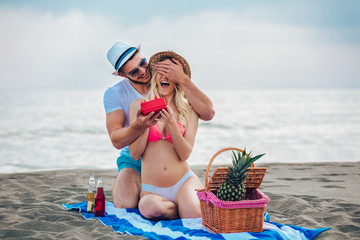 Young man suprising his girlfriend with gift on the beach