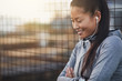 © Flamingo Images - Smiling Asian woman in sportswear standing outdoors listening to