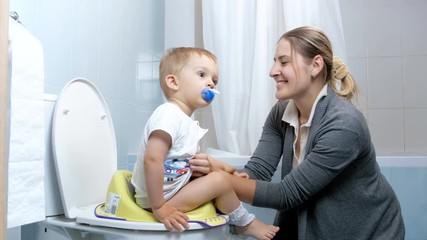 Wall Mural - 4k footage of young mother talking and singing while teaching her baby son using toilet