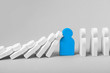 © adragan - Concept of domino effect in business. The fall of the crumbling business is saved by special employee leader. The line of dominoes from the white figures of the man is falling, one blue man stops fall