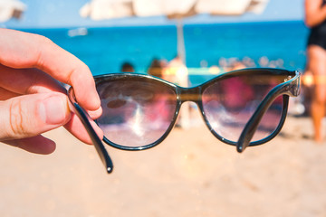 Wall Mural - Sunglasses in a hand on the beach, bright summer day