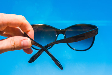 Wall Mural - Sunglasses in a hand on the beach, bright summer day