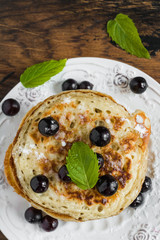 Wall Mural - Sweet pancakes with black currant and powdered sugar on white plate on wooden rustic table, top view, close-up.