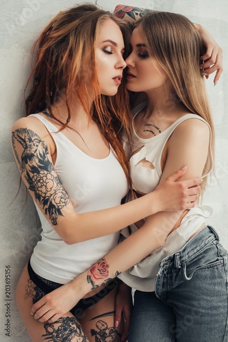 Fotografía Tattooed sexy girls embracing shot against wall
