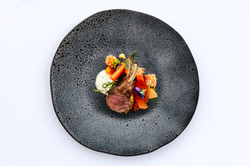 Modern French cuisine: Close up roasted Lamb neck & rack served with carrot, yellow curry served in black stone plate.