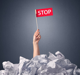 Wall Mural - Female hand emerging from crumpled paper pile holding a red flag with stop written on it 