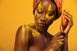 © Mike Orlov - Cheerful young african woman with yellow makeup on her eyes. Female model against yellow background with orange flower.