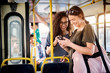 © dusanpetkovic1 - Two gorgeous joyful young women are together looking at phone and laughing while standing in a bus.