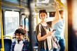 © dusanpetkovic1 - Young beautiful woman is standing in the bus using phone and holding onto the bar while waiting to arrive at her destination.