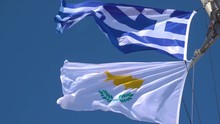 Waving Greek And Cyprus Flags Agaist The Blue Sky In Strong Wind