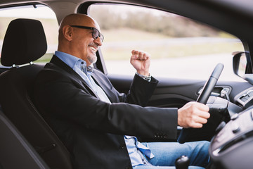 Mature cheerful professional elegant businessman in a suit is driving a car and laughing.