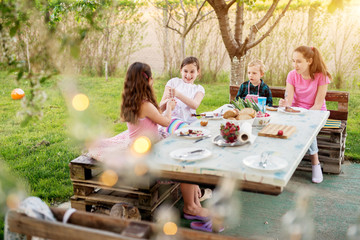 After they finished meat from the stick , two playful girls are having a sword fight with sticks while their older sister and toddler brother are watching them.