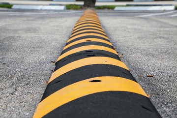 Yellow and Black Striped Speed Bump with Nails Visible in Parking Lot with Diagonal Spaces, White Blocks and Green Grass Above in Background