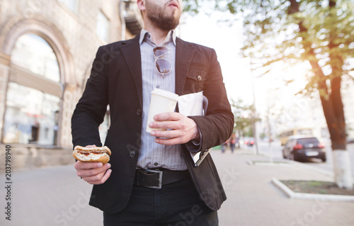 Fotografía A businessman walking down the street with a snack and coffee in his hands