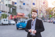 © bodnarphoto - Portrait of a handsome businessman with a cup of coffee against a background of blurred urban landscape. A solid man with a beard stands against the backdrop of roads and cars