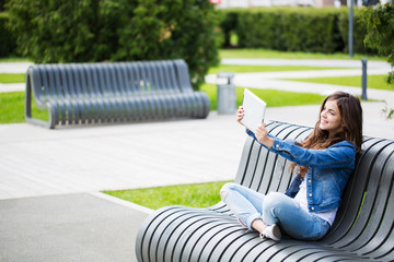 Wall Mural - Beautiful girl student holds a laptop sitting on bench.