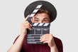 Professional male actor ready for shooting film, holds movie clapper, prepares for new scene, wears special clothes, isolated on white background. Handsome young man poses with clapboard in studio