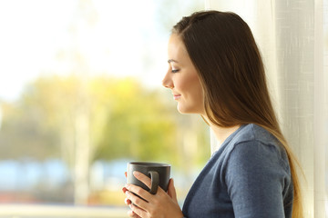 Wall Mural - Pensive lady holding a coffee mug beside a window