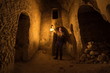 Man with kerosene lamp explores ancient abandoned underground chalky cave temple. 