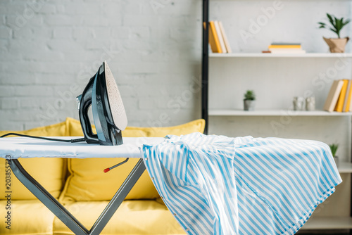 Fotomural striped blue shirt and iron on ironing board at home