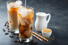 Ice Coffee In A Tall Glass With Cream Poured Over, Brown Sugar And Coffee Beans. Cold Summer Drink On A Dark Background. With Copy Space