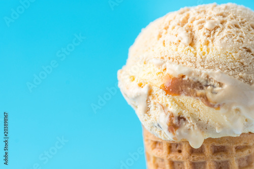 Fotografía Scoop of Delicious Melting Salted Caramel Toffee Vanilla Ice Cream in Waffle Cone on Blue Background