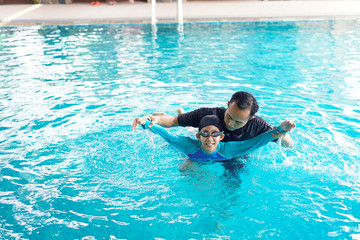 Wall Mural - Father teaching daughter to swim in a swimming pool