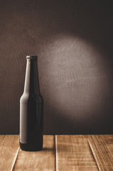 Wall Mural - black bottle of beer on a dark background/black bottle of beer on a dark background of a wooden shelf. Selective focus and copyspace