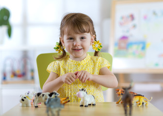 Poster - child girl playing with animal toys at table in kindergarten or home