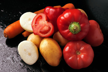 Red sweet pepper, tomatoes, carrots, onions and potatoes on a black background