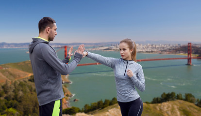 Wall Mural - fitness, sport, martial arts and people concept - happy woman with personal trainer working on strike over golden gate bridge in san francisco bay background