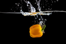 Yellow Pepper Falling Into Water And Splashing Against Black Background