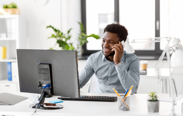 business, people, communication and technology concept - smiling african american businessman with computer calling on smartphone at office