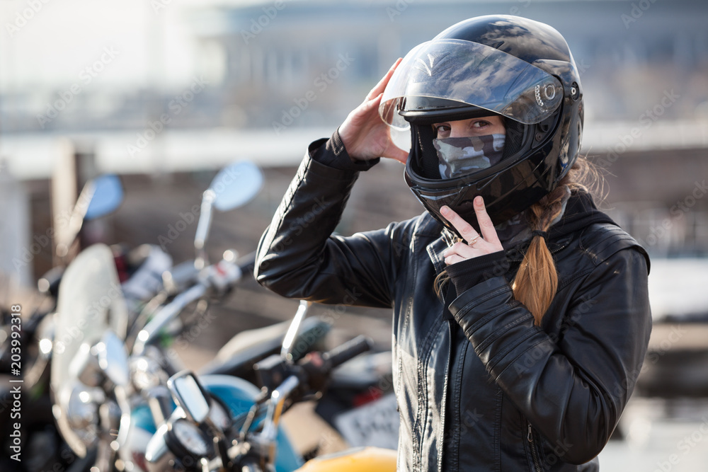 Stock Foto Young girl biker trying black motorcycle helmet for ride on bike Adobe Stock