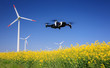 Inspection drone with eolian turbines behind. Rapeseed field in bloom. Renewable energy.